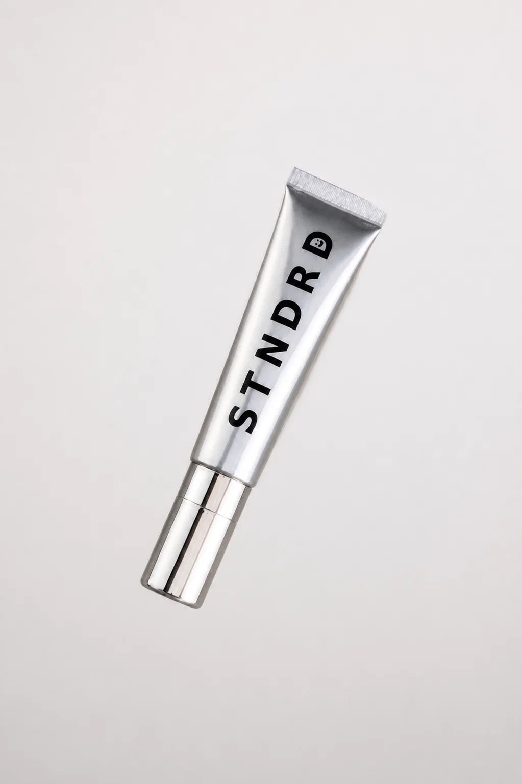 STNDRD lip balm tube lying at an angle on a light grey surface