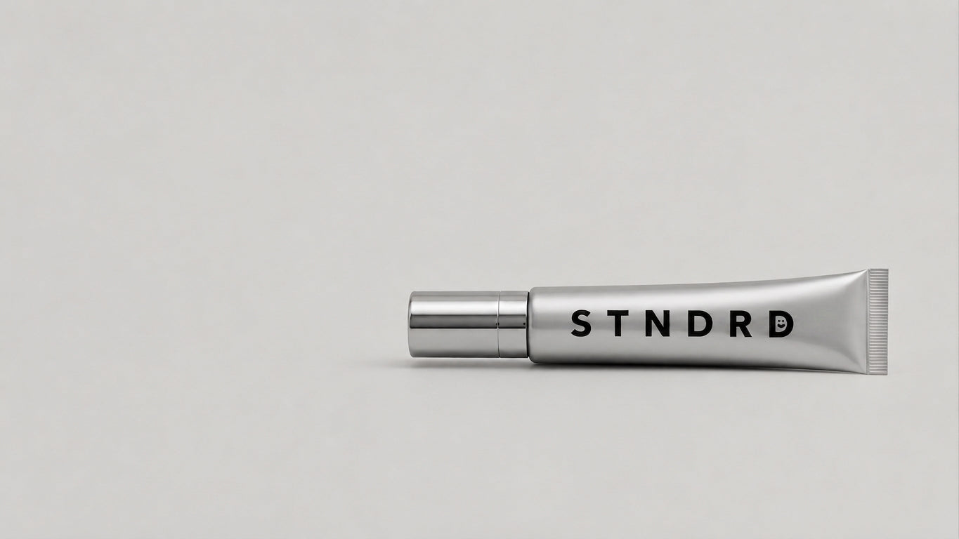 STNDRD lip balm tube resting diagonally on a light grey surface
